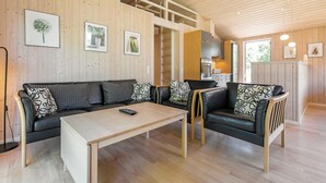 Ein gemütliches Wohnzimmer mit einer Couch, Sesseln, einem Couchtisch und einem durch eine offene Tür einsehbarer Küchenbereich.