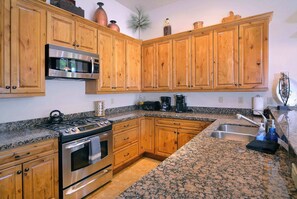 Eine Küche mit Holzausstattung, Edelstahlgeräten, Granitarbeitsplatten und einer Granit-Spritzschutzwand.