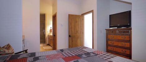 Un dormitorio con cama, tocador, televisión y baño visible a través de una puerta abierta.