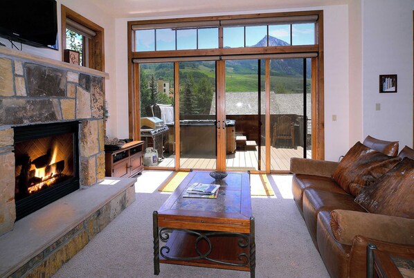 A living room with a stone fireplace, a wooden coffee table, a leather sofa, and a large sliding glass door leading to an outdoor patio.