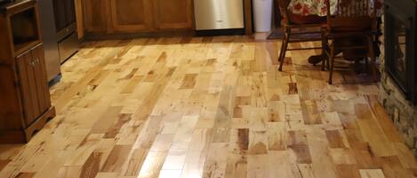 A kitchen with wooden flooring, wooden cabinets, a dishwasher, and a dining area with a chair and table.