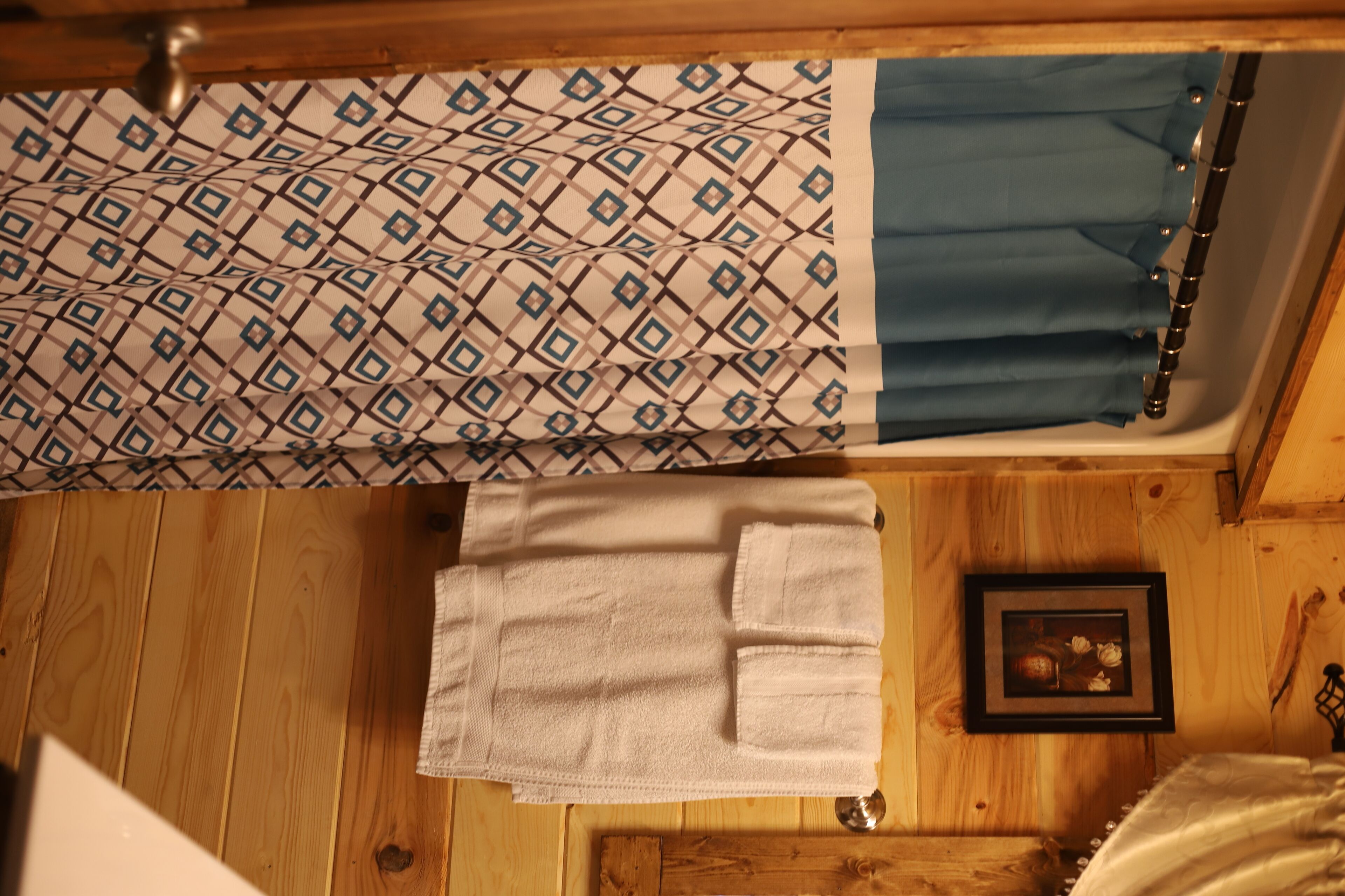 A room with a wooden floor, a bed with a patterned bedspread, a blue curtain, and a framed picture on the wall.