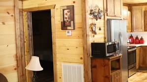 Interior de una cabaña de madera con zona de cocina equipada con refrigerador, microondas y estufa.