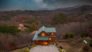 Una cabana de fusta amb teulada verda, envoltada per fullatge d'octubre i un cel nocturn estrellat.