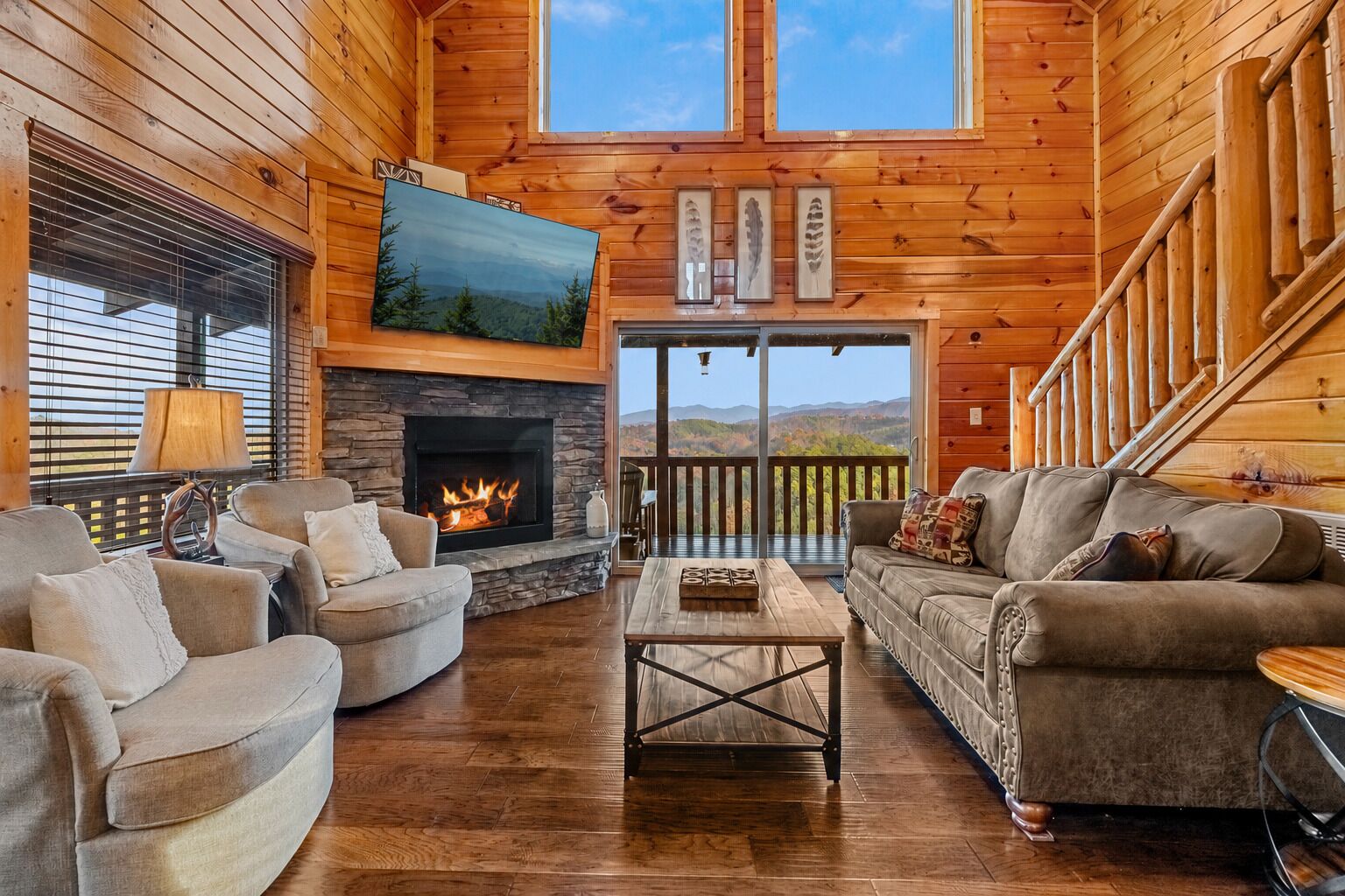 A cozy cabin interior with a stone fireplace, comfortable seating, and a large window overlooking a scenic landscape.
