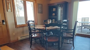 A dining area with a wooden table and chairs, a dark wooden cabinet, and a view of the outdoors through a window. - Holiday Lodge on Green Bay (Sturgeon Bay)
