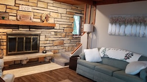 A cozy living room with a stone fireplace, a sofa with decorative pillows, and a painting on the wall. - Holiday Lodge on Green Bay (Sturgeon Bay)
