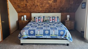 A bedroom with a wooden ceiling, a bed with a lighthouse-themed quilt, two nightstands with lamps, and a ceiling fan. - Holiday Lodge on Green Bay (Sturgeon Bay)