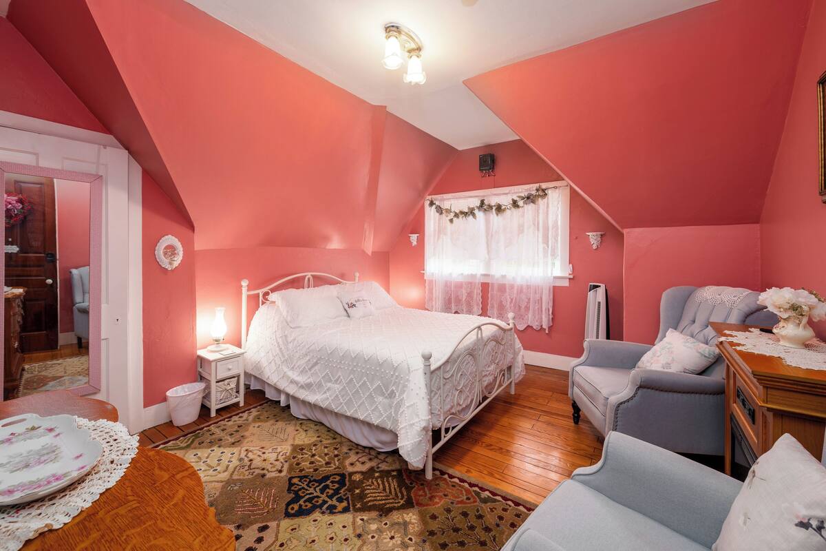 A bedroom with a bed, a chair, a nightstand, a lamp, and a window with curtains.