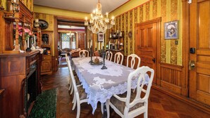 A dining room with a long table, white chairs, a chandelier, and wooden paneling. - Gillis Grier Bed & Breakfast (Salisbury)