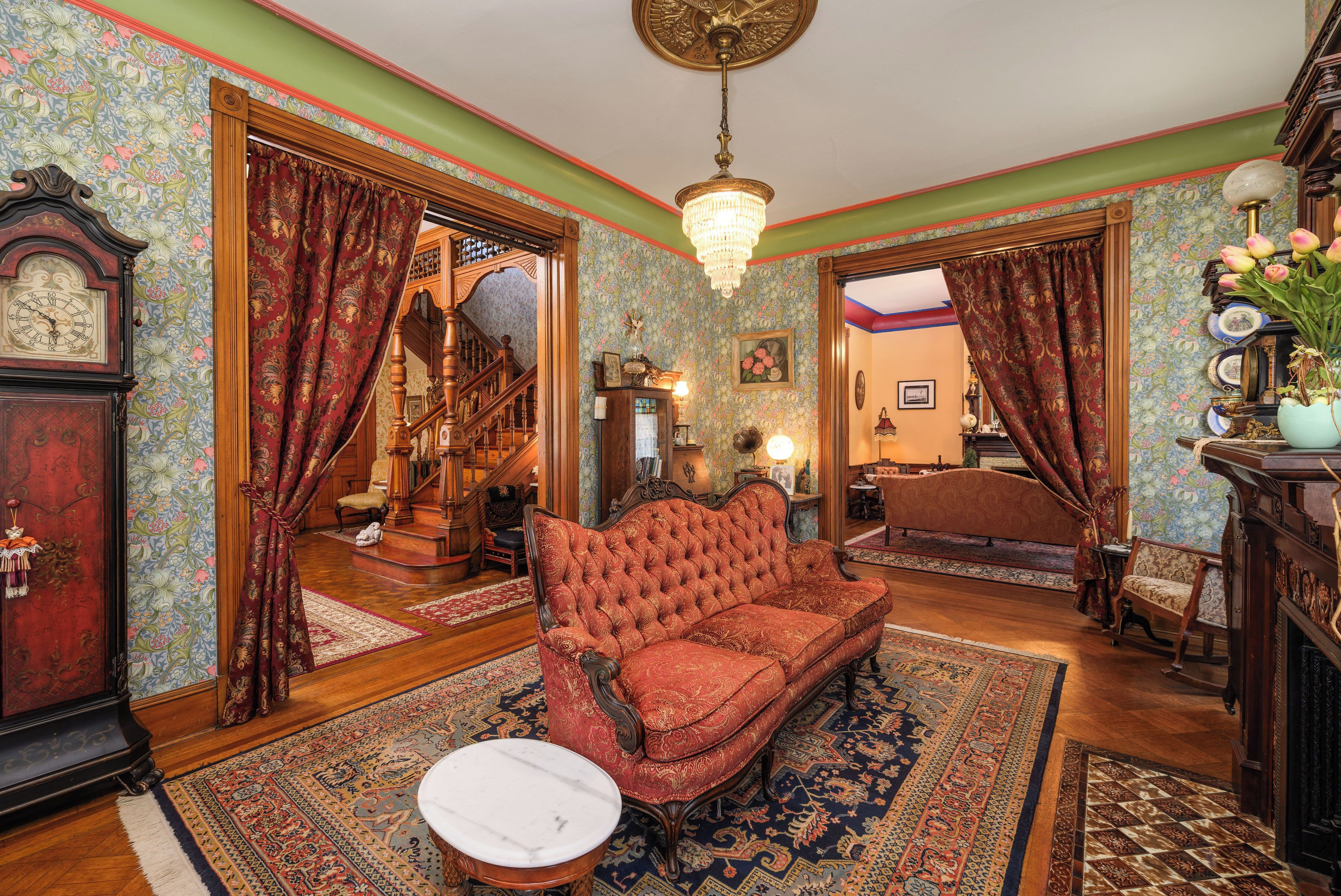 A room with a vintage sofa, a wooden floor, a chandelier, and a clock.