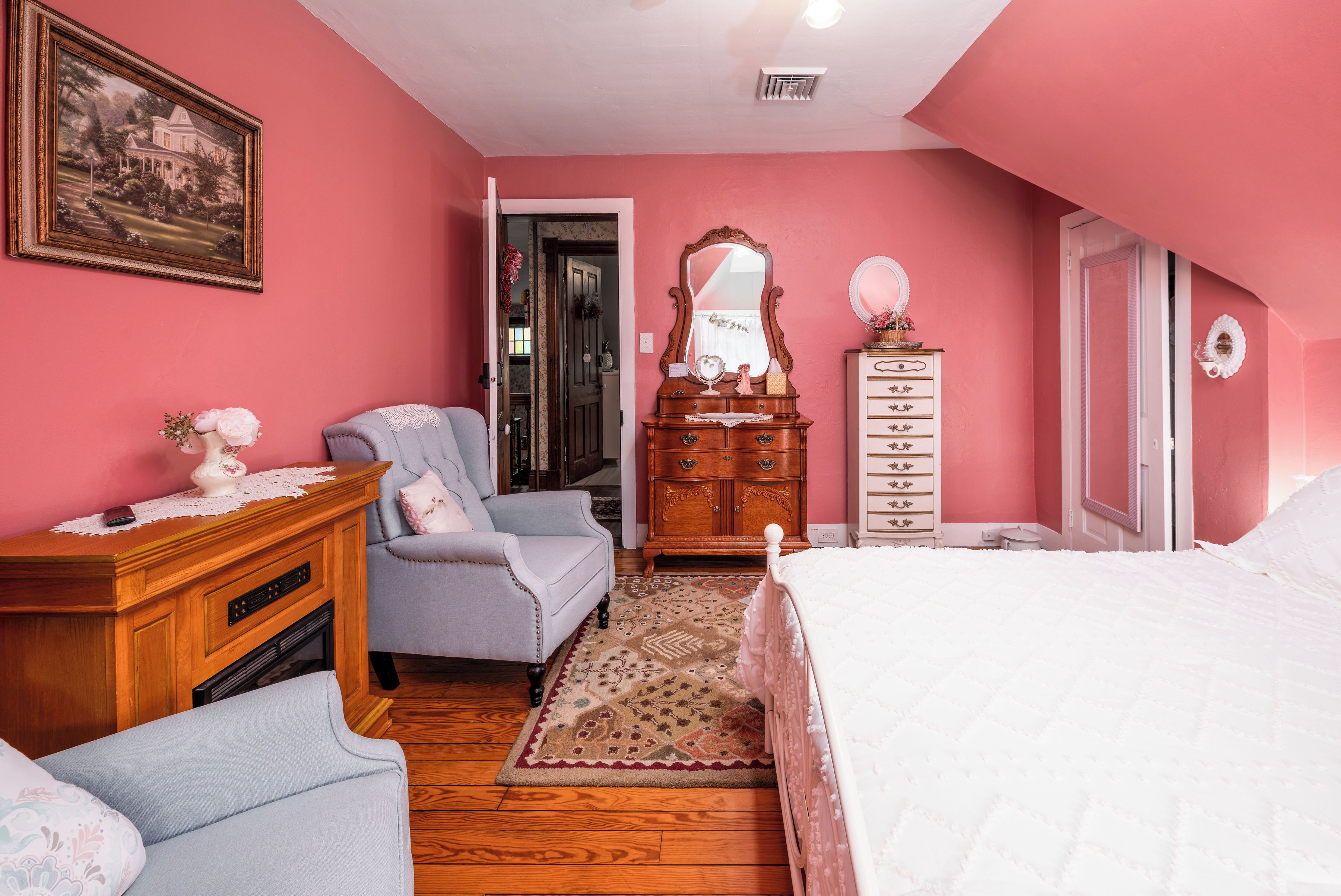 A bedroom with pink walls, a wooden dresser, a white bed, a chair, and a rug.