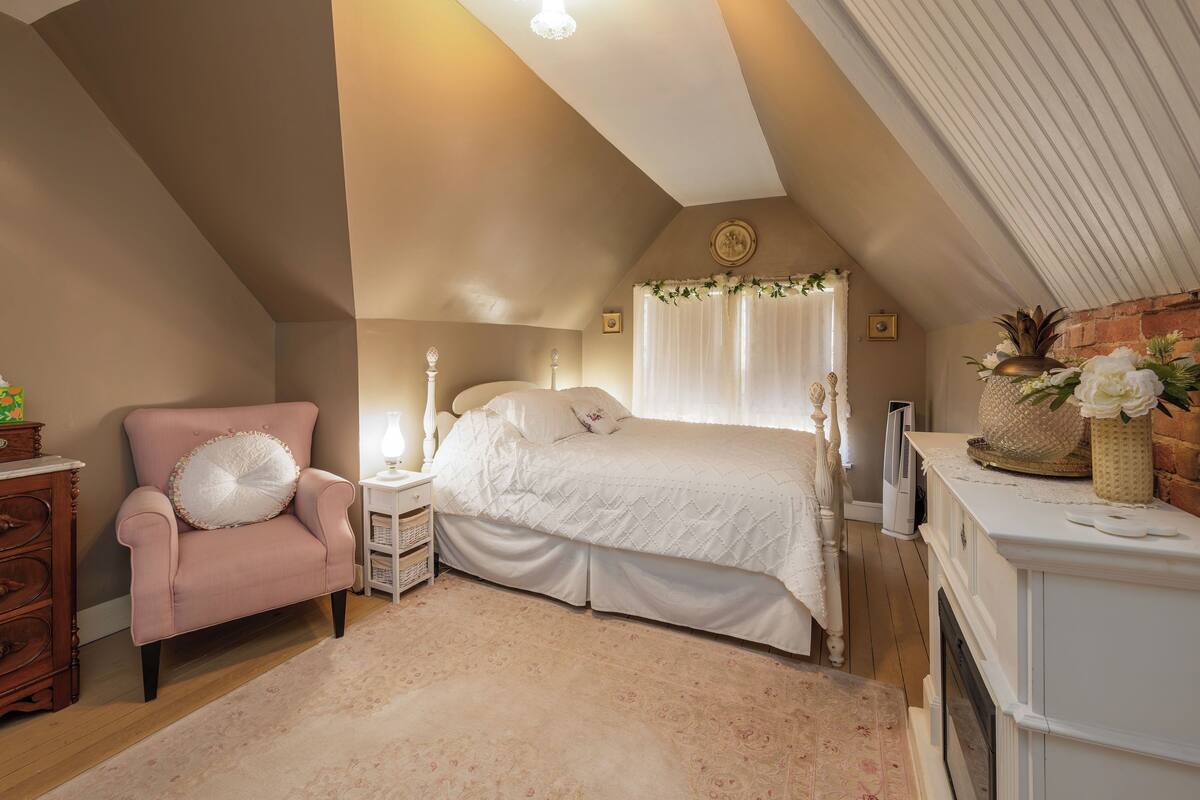 A bedroom with a bed, a chair, a nightstand, a dresser, and a fireplace.
