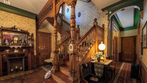 A grand staircase with ornate woodwork, a fireplace with a checkered floor, and a cozy seating area with a lamp. - Gillis Grier Bed & Breakfast (Salisbury)