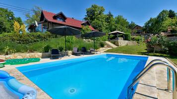 A swimming pool with lounge chairs and umbrellas, surrounded by a stone wall and greenery.
