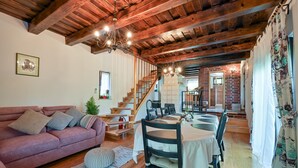 Una sala de estar acogedora con techo de madera, un sofá rosa, una mesa de comedor con sillas y una escalera que lleva a otra habitación.