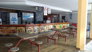 Un restaurante con una barra que exhibe imágenes de comida, un refrigerador con la marca 'Golo Caldas' y un piso de baldosas.