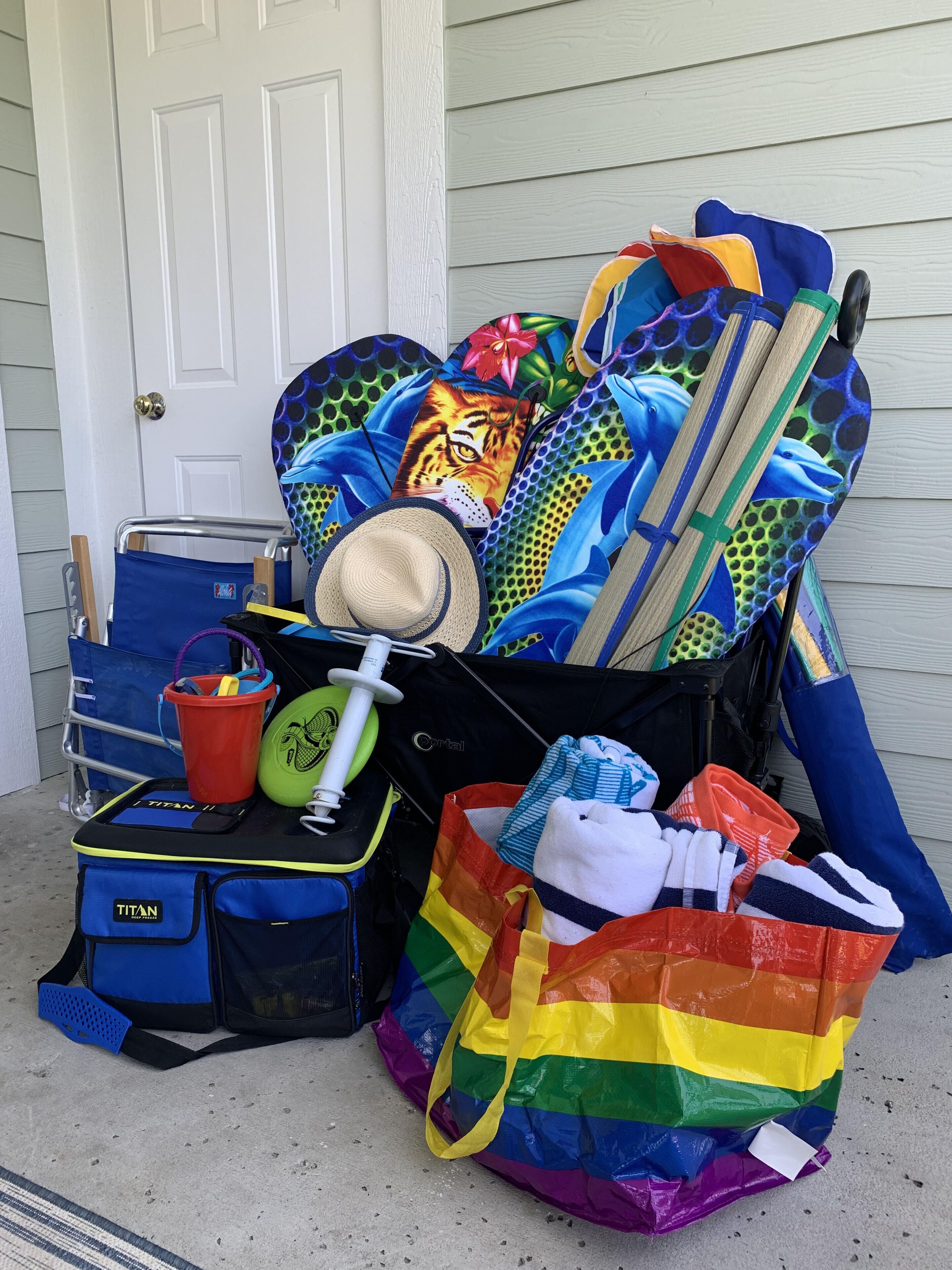 A collection of colorful beach gear and a rainbow bag outside a house.