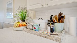 Un plan de travail de cuisine avec un panier de fruits, une plante en pot, un pot à épices, un pot blanc et un plateau contenant des ustensiles.