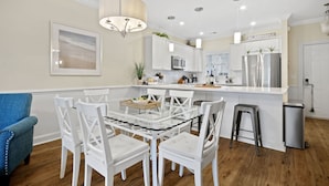 Une cuisine moderne avec des meubles blancs, un îlot central et un coin repas avec des chaises blanches.