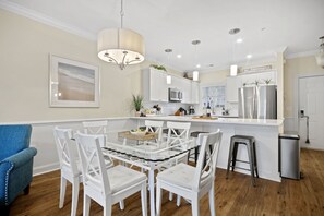 Una cocina moderna con armarios blancos, una isla central y una zona de comedor con sillas blancas.