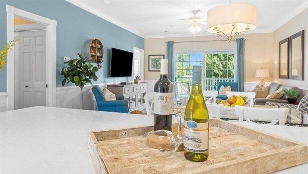 Un salon moderne doté d’un grand îlot central blanc, d’un coin repas avec une chaise bleue et d’une cuisine en arrière-plan.