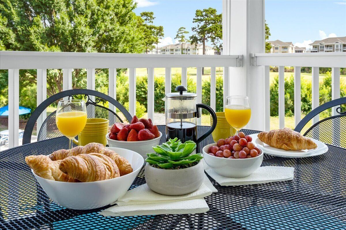 A breakfast setup on a balcony with croissants, fresh fruits, a coffee pot, and glasses of orange juice.
