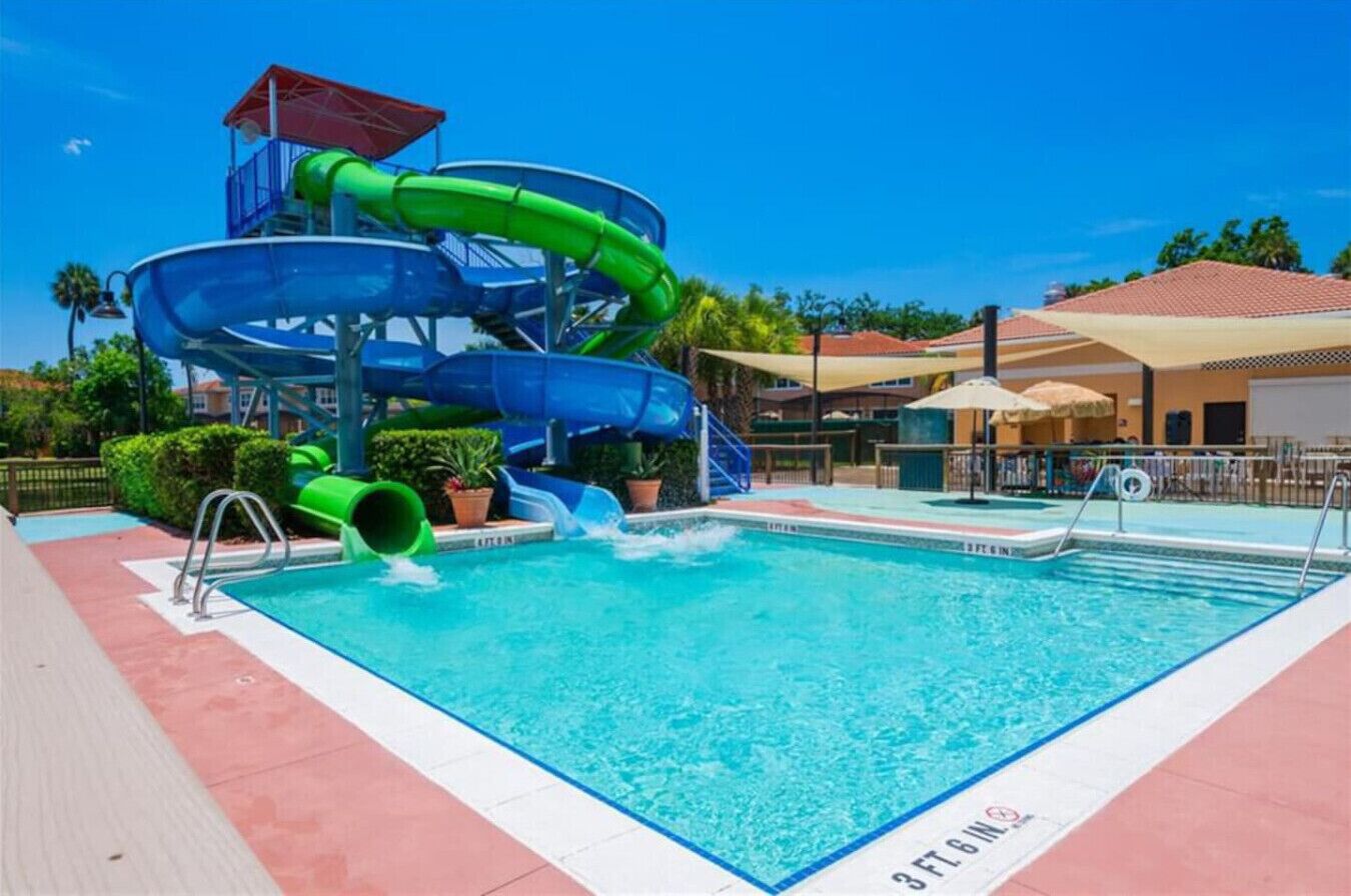 A pool with a water slide, a lifeguard stand, and a poolside area with umbrellas.