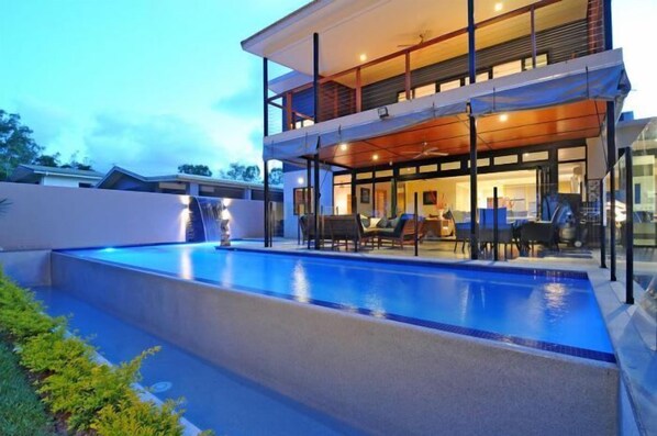 A modern two-story house with a swimming pool, outdoor seating, and a covered patio area.