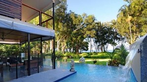 A swimming pool with a waterfall feature, surrounded by lush greenery and a modern building structure.