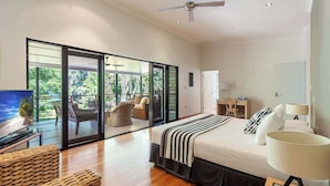 A modern bedroom with a large bed, a TV, a desk, and a balcony with a view of greenery.