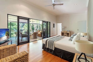Un dormitorio moderno con una cama grande, televisión, escritorio y balcón con vistas a zonas verdes.