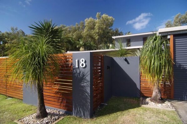 A modern house with a number 18 sign, a wooden fence, and two palm trees.