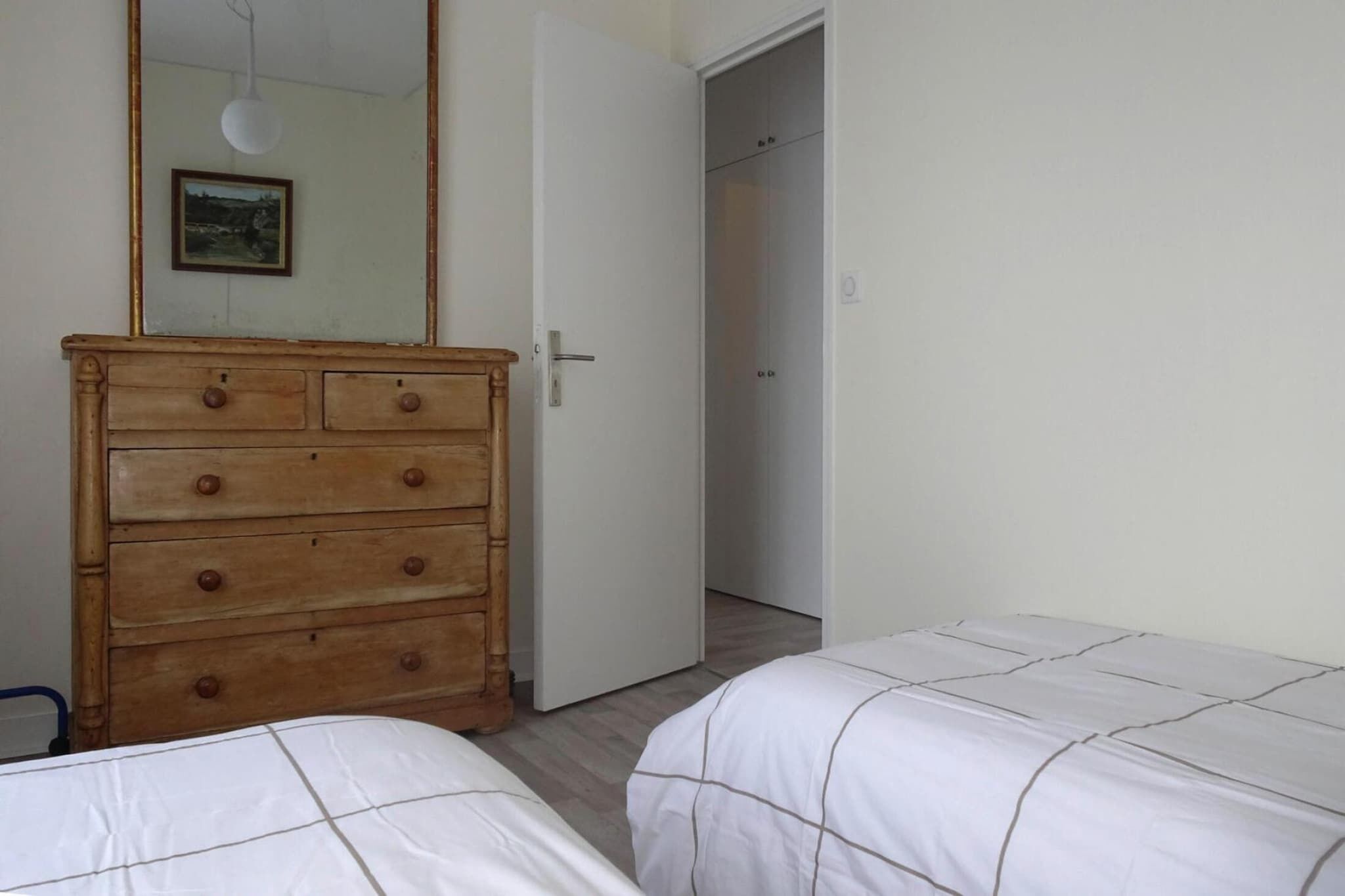 Un dormitorio con un aparador de madera, dos camas con ropa blanca, un espejo y una puerta que da a otra habitación.