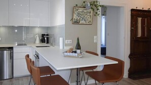 A modern kitchen with white cabinets, a white dining table, and four brown chairs. There is a bottle of champagne on the table. - Apartment in Fouesnant by Sandy Cove (Beg Meil)