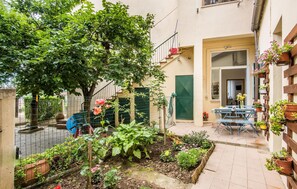 Un patio con jardín, una mesa con sillas y un edificio con puerta verde.