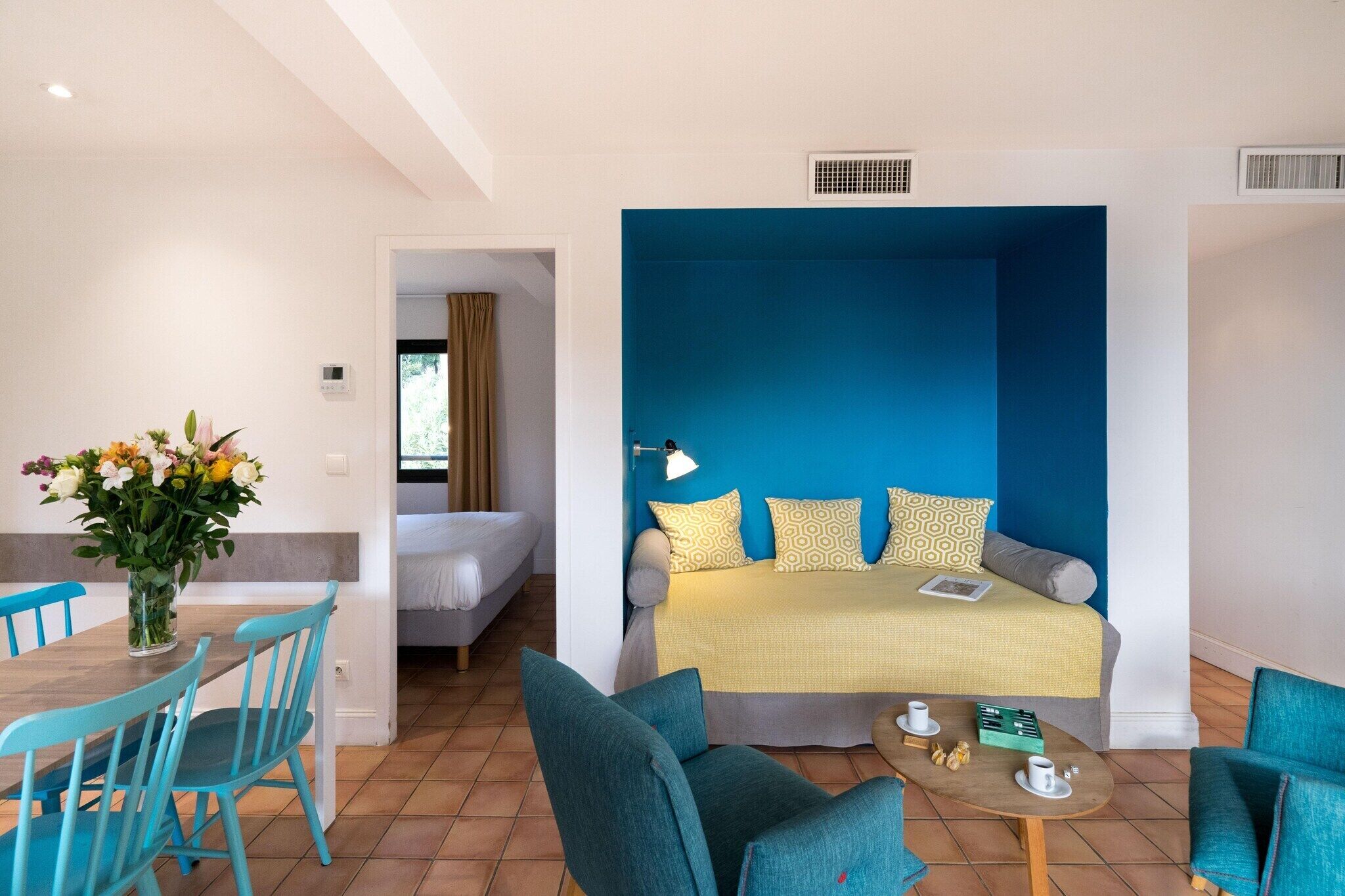 Una stanza con un letto, un divano, un tavolo da pranzo con sedie e un vaso di fiori.