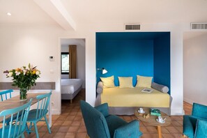 A room with a bed, a sofa, a dining table with chairs, and a vase of flowers. - Apartment in Saint-Tropez with Beach Access (Rayol-Canadel-sur-Mer)