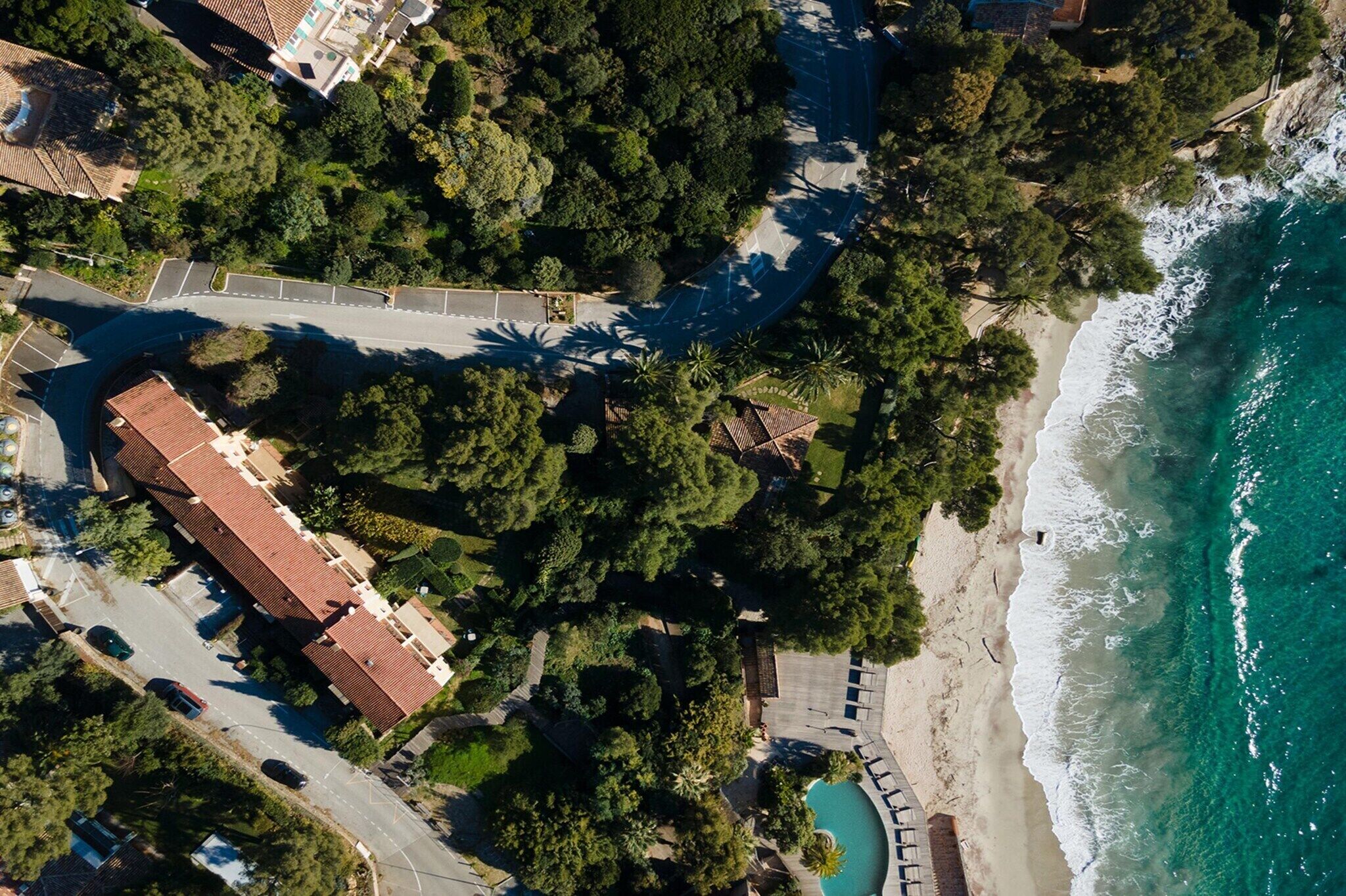 An aerial view of a coastal area with a beach, a road, and a building with a red roof.