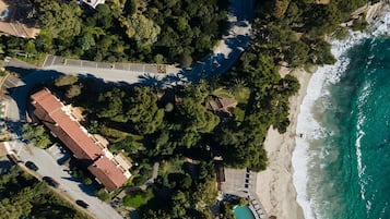 An aerial view of a coastal area with a beach, a road, and a building with a red roof.