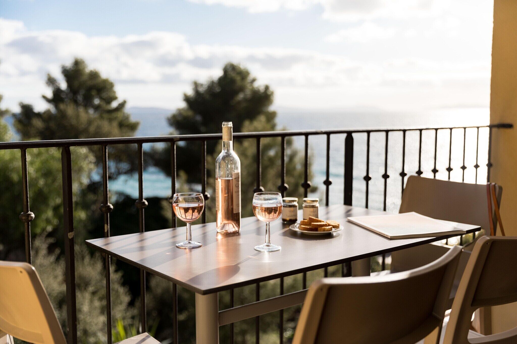 A balcony table with a bottle, glasses, and a plate of bread.