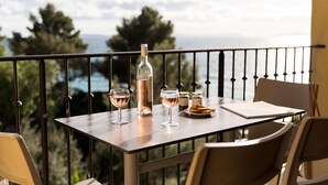 A balcony table with a bottle, glasses, and a plate of bread. - Apartment in Saint-Tropez with Beach Access (Rayol-Canadel-sur-Mer)