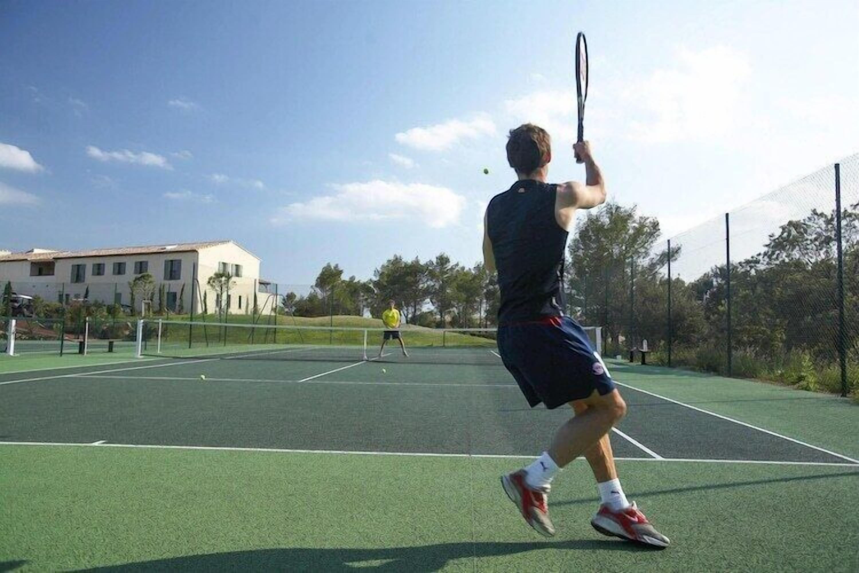 Een tennisbaan met een net, twee spelers en een gebouw op de achtergrond.