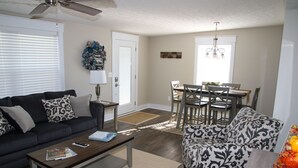 A living room with a sofa, coffee table, and patterned armchair. There is a dining area with a table and chairs. - Gray's Landing- NEWLY Renovated / 1.8 miles to the ARK! (Williamstown)