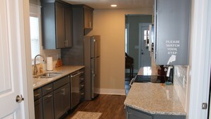 A kitchen with wooden flooring, dark cabinets, a granite countertop, and a refrigerator. - Gray's Landing- NEWLY Renovated / 1.8 miles to the ARK! (Williamstown)