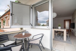 An open balcony with a table and chairs, a sliding door, a TV, and a stone wall.