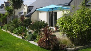 Una casa residencial con un jardín cuidado, una sombrilla azul y diversas plantas.