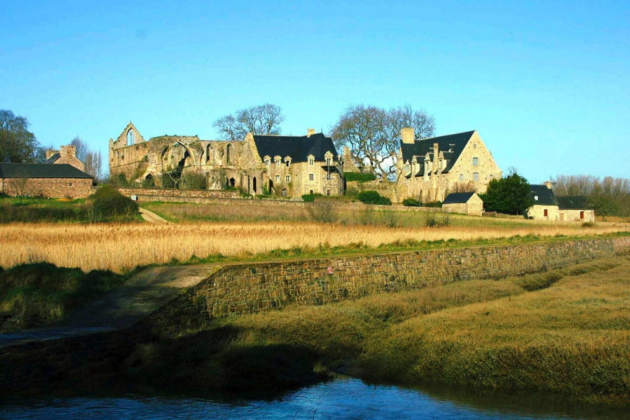 Ein historisches Steinhaus mit Rundbogenfenstern und einem steilen Satteldach, gelegen am Wasser.