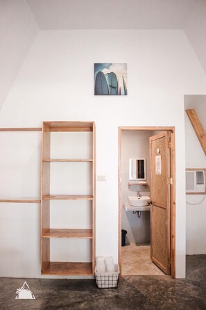 A room with a wooden wardrobe, a white wall, a framed picture, a wooden door leading to a bathroom, and a small basket on the floor. - Triangle Palms Siargao (General Luna)