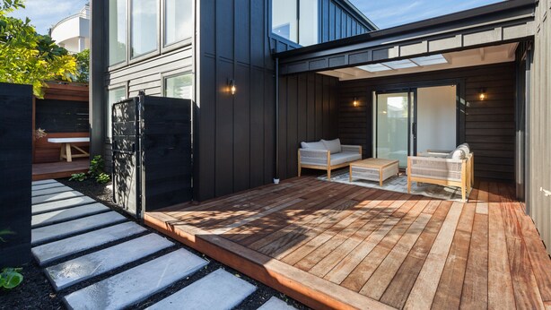 Una casa moderna con terraza de madera, un patio cubierto y puerta corrediza de vidrio que da a un área de estar al aire libre.